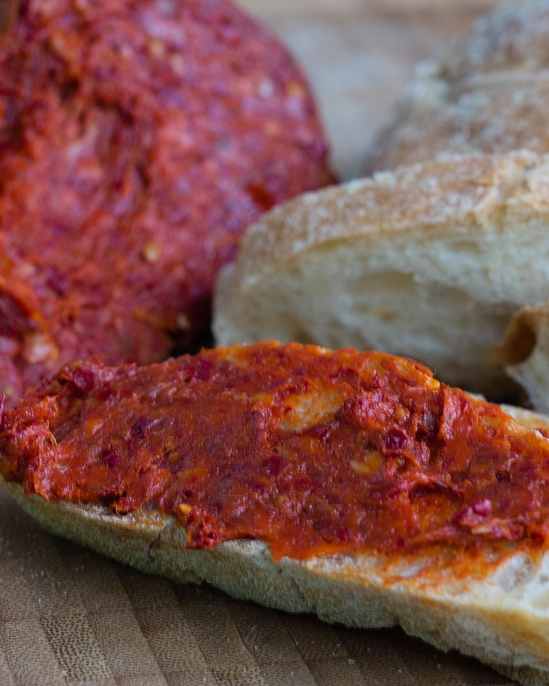 'Nduja calabrese spalmata su una fetta di pane, dietro il salume intero e altro pane